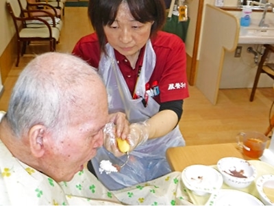 職員が高齢者の食事を支援している風景。介護の日常的なケアシーンを示している。